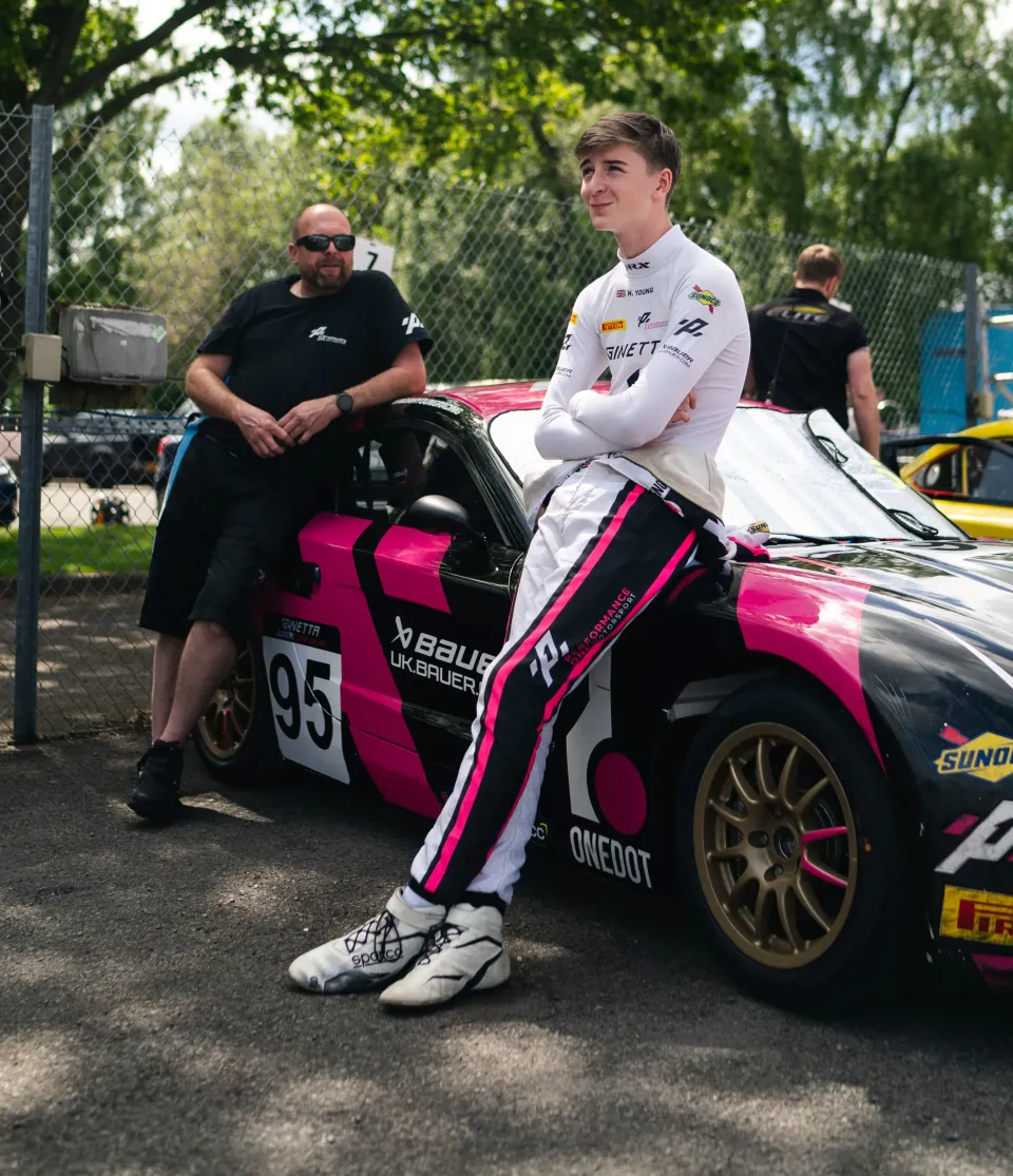 Noah Young in his race suit beside his number 95 Ginetta in the paddock