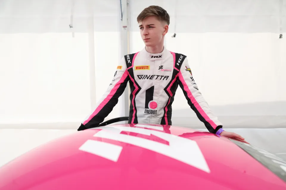 Noah Young in his Ginetta race suit leaning on his car in the team awning